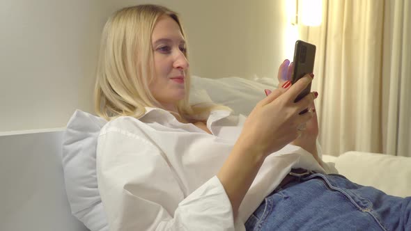 a woman at home reads a text message on her smartphone while lying on the bed. alt