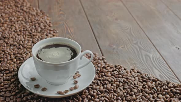 Black Coffee in a White Cup with Spinning Bubbles on a Flat Wooden Surface Partially Covered with