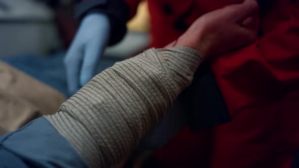 Closeup Ambulance Paramedic in Gloves Wrapping Patient Hand with Elastic Bandage alt