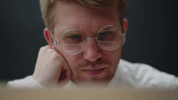 Portrait of a Tired Pensive Man Looking at a Laptop Screen with Glasses alt