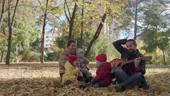 Family with Young Children Relaxing in the Park Picnic Spending Time Together Dad Playing Guitar