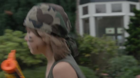 Young boy playing soldier with toy gun running through beautiful suburban neighborhood alt