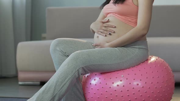 Expecting Female Sitting on Fitness Ball, Holding Hands on Stomach, Relaxation alt