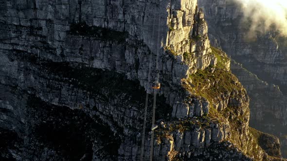 Cinematic aerial shot of a cable car descending down the cliffs of a mountain