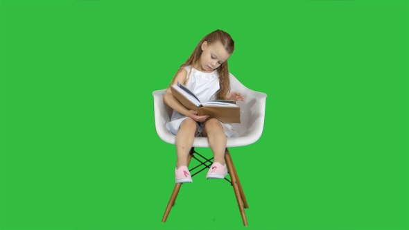 Little Student Girl Sitting and Reading Book on A Green