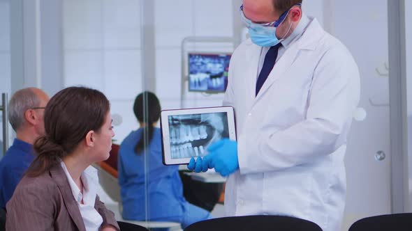 Woman Sitting on Chair Listening Doctor Looking on Tablet with Xray alt