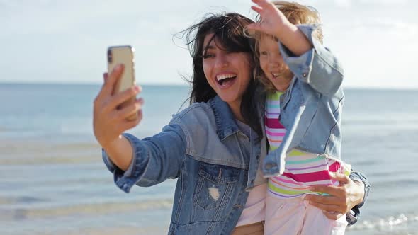 Mother and Daughter Talking Online By Video Call on Cellphone in Summer Sea. Portrait of Smiling alt