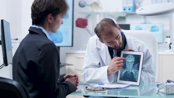 Male Doctor Showing To an Young Female Patient a X Ray Scan on a Tablet alt