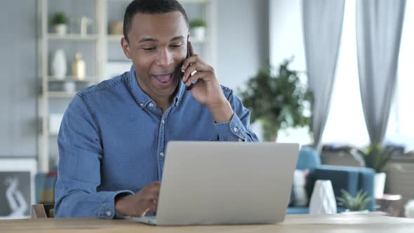 Young African Man Talking on Phone at Workplace alt