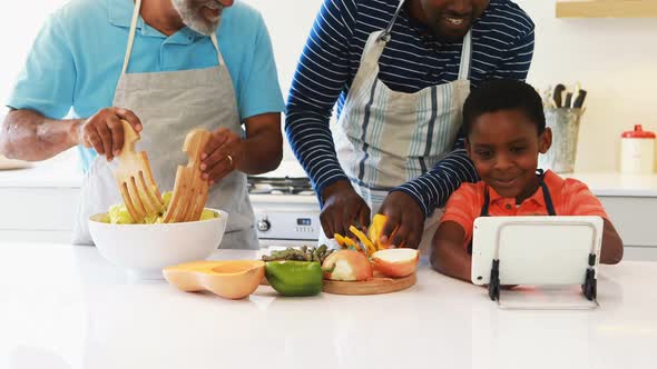 Boy showing digital tablet to his father and grandfather while preparing salad alt