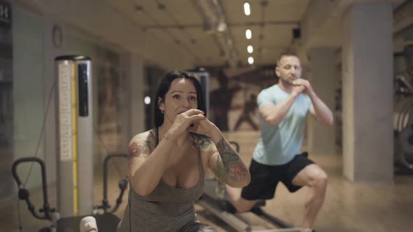 Attractive Female Personal Trainer Showing Exercise To Blurred Man Repeating at the Background alt