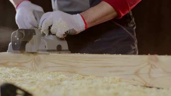 Close-up Hands of Joiner Using Electric Planer with Wooden Blank in Workshop. alt