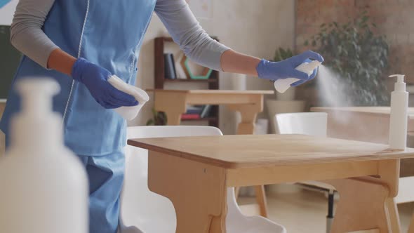 Janitress Using Sanitizing Spray and Wiping School Desks in Classroom alt
