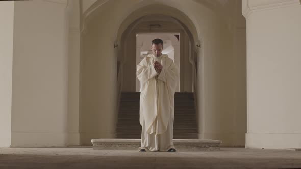 Priest in White Robe Praying to God at Church Entrance alt