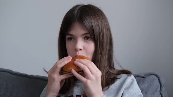 Little Girl Teenager Eating Burger at Home on the Couch