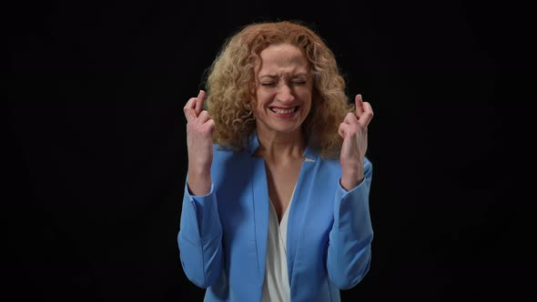 Woman Crossing Fingers in Hope Gesture Closing Eyes Praying at Black Background alt