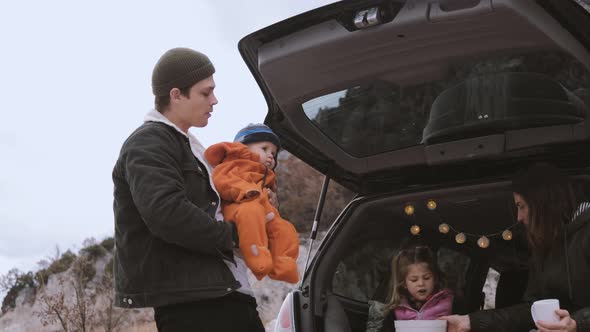Traveler Family  sitting in the open trunk of a black car with kids near bonfire alt
