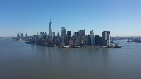 An aerial view of New York Harbor on a sunny day with blue skies. The drone camera facing lower Manh alt