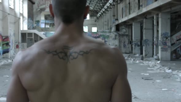 The back of a shirtless personal trainer man does a workout inside an abandoned building. alt