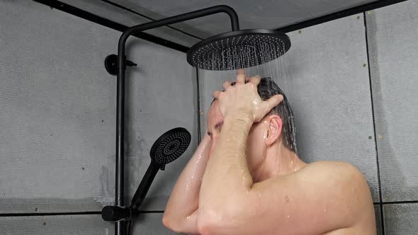 Young Man Takes Shower Washing Hair Under Cold Water at Home alt