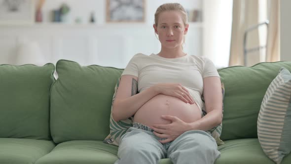 Pregnant Woman Looking at Camera While Holding Her Tummy alt