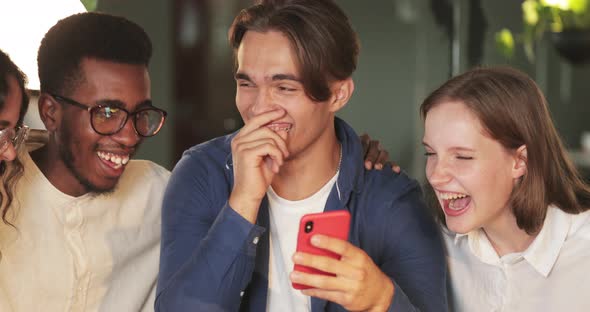Happy Multiethnic Friends Looking at Smartphone Screen and Laughing. Group of Young Cheerful People alt