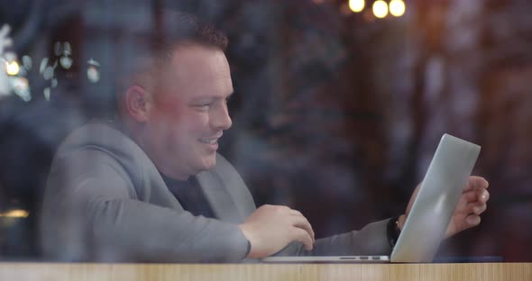 Joyful Man Leads A Video Conference From A Cozy Cafe. Rejoices In The Achievements Of Employees