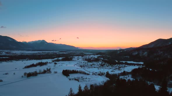 Drone shot of mountains, fields, and landscape in winter at golden hour, sunrise with snow, flying o alt