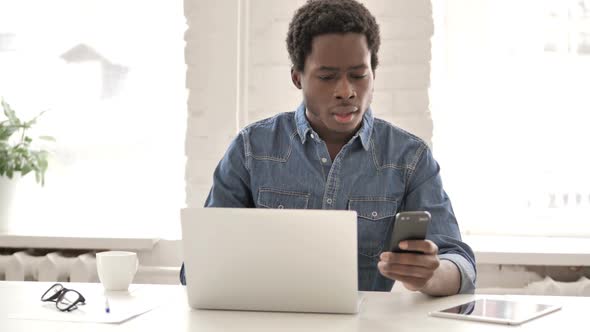 African Man Using Phone and Laptop for Information alt