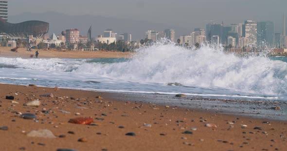 60FPS: Waves crash on beach in Barcelona with a beautiful skyline in the background - mid shot alt
