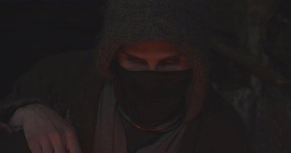 Hooded And Masked Figure In Cave Staring Fire alt