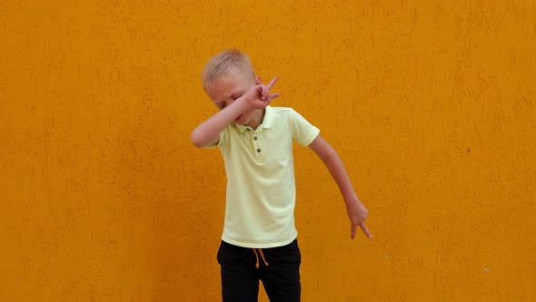 A Little Cheerful Boy Jumps and Has Fun Against the Background of a Yellow Wall alt