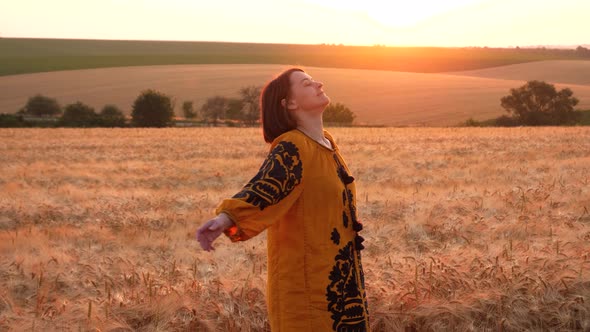 young woman in Ukrainian traditional clothes at golden field by sunset light
