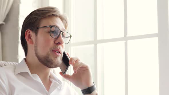Portrait of Young Man Freelancer Talking on Smartphone Sitting in Home Office