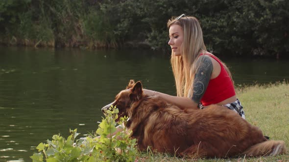 Younng Woman Petting Her Border Collie Dog While Sitting on Grass in Park