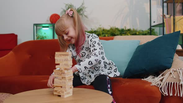 Funny Happy One Teenage Kid Girl Play Wooden Tower Blocks Bricks Game at Home in Modern Living Room alt