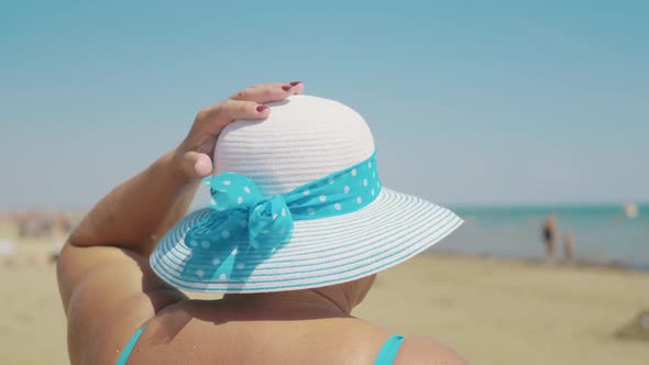 Happy Senior Woman in Sun Hat on Summer Beach. Age, Leisure and People Concept. Back View. alt