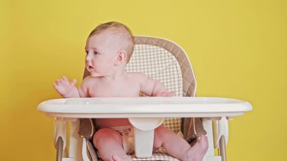 Mother feeding toddler baby from a spoon on a high chair for children, studio yellow background