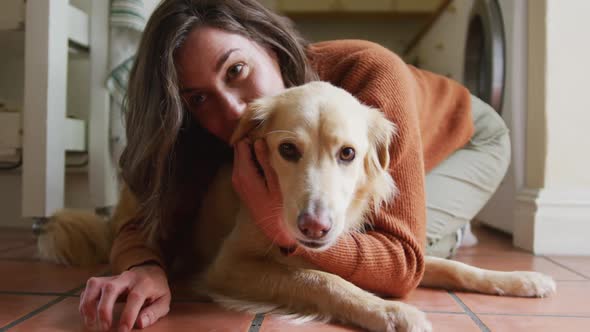 Smiling caucasian woman kissing and cuddling her pet dog sitting on floor at home alt
