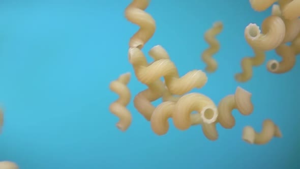Closeup of the Pasta Cellentani Falling Down on a Blue Background alt