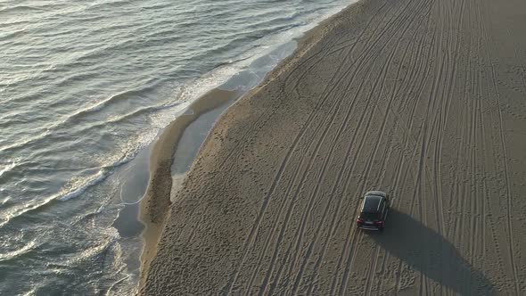 Aerial View of a Car Moving Along a Sandy Beach Along the Sea