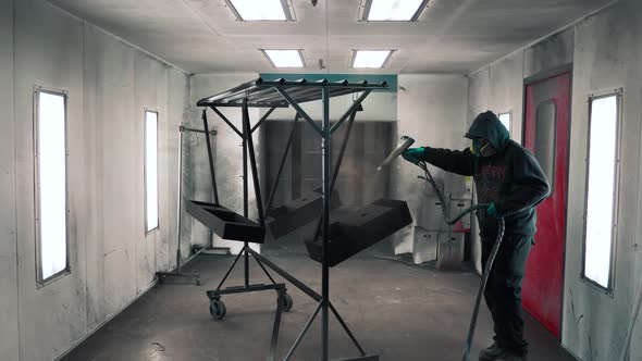 Man applying black anti-corrosion powder coating to metal sheet using a spray gun in factory. alt