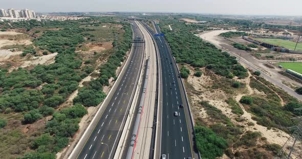 A train travels near the highway towards the city. alt