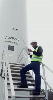 A Man in a Work Uniform is Diagnosing a Wind Turbine Using a Digital Tablet alt