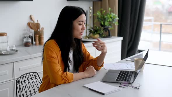Friendly Pretty Asian Brunette Girl Manager Freelancer Sit in the Kitchen Uses Laptop Talking By alt