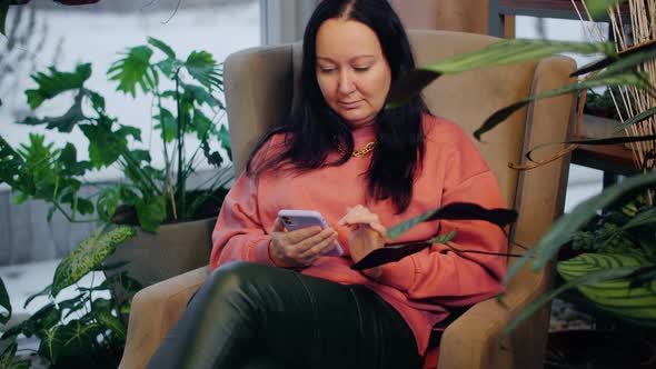 Woman Using Smartphone While Sitting Near Green Plants Indoors alt