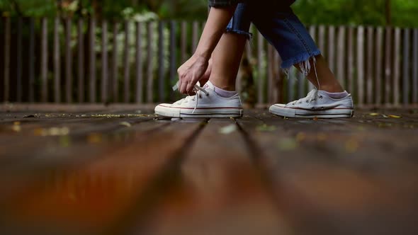 Young Asian woman trying on white sneakers at a public park on a rainy day.