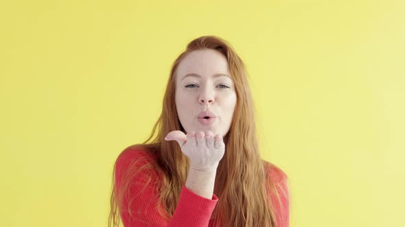 Caucasian cheerful woman with red hair in a good mood blows kiss to camera