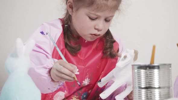 Little girl painting paper mache figurine at homeschooling art class. alt