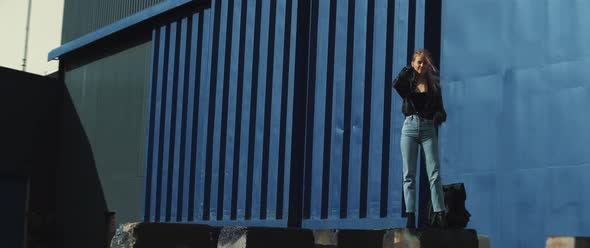 Young woman looks around standing in front of a huge metal container alt